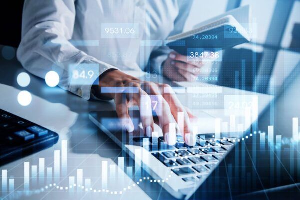 شخص يستخدم جهاز الحاسوب المحمول، وخلفية مليئة بالأرقام والرسوم البيانية المالية.